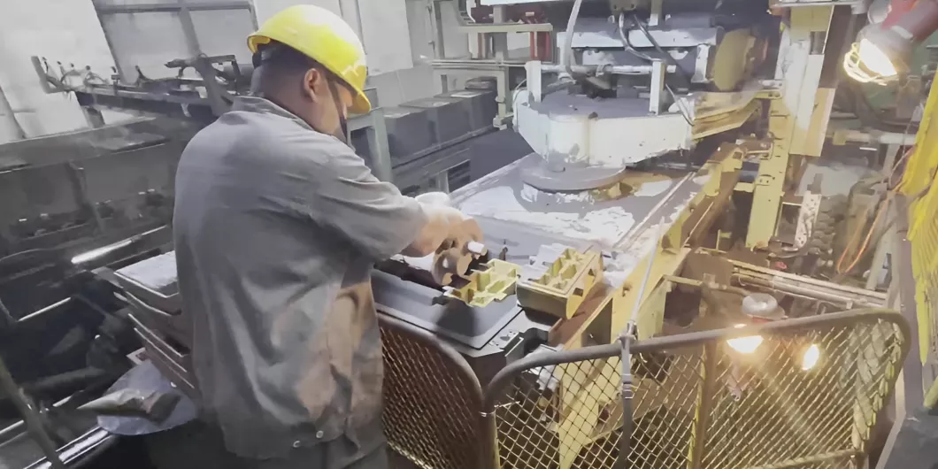 Workers wearing helmets take castings out of sand molds